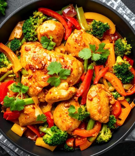 A vibrant and healthy chicken and vegetable stir-fry, featuring broccoli, bell peppers, and carrots, cooked to perfection in a black skillet, garnished with fresh cilantro.