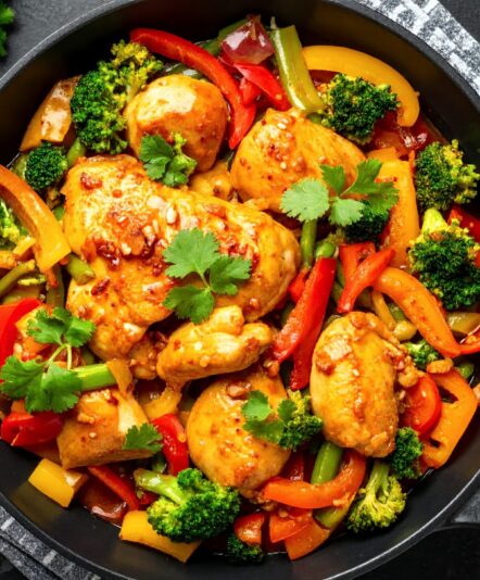 A vibrant and healthy chicken and vegetable stir-fry, featuring broccoli, bell peppers, and carrots, cooked to perfection in a black skillet, garnished with fresh cilantro.