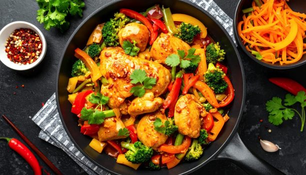 A vibrant and healthy chicken and vegetable stir-fry, featuring broccoli, bell peppers, and carrots, cooked to perfection in a black skillet, garnished with fresh cilantro.